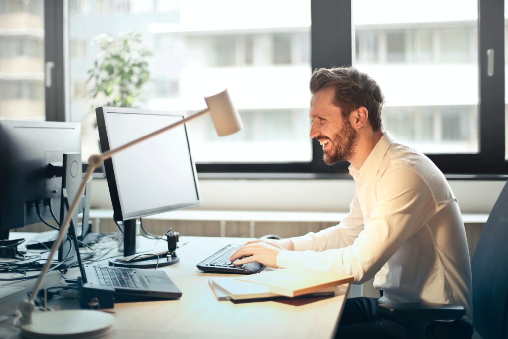 Smiling man sitting at a desk with two monitors