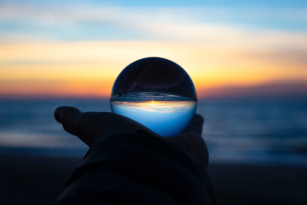 A hand holding a crystal ball on a beach at sunset